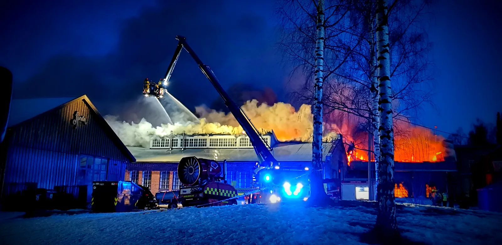18:18. Mørkt, blålys og lift. Hele takrekka brenner bak bjørkene.
