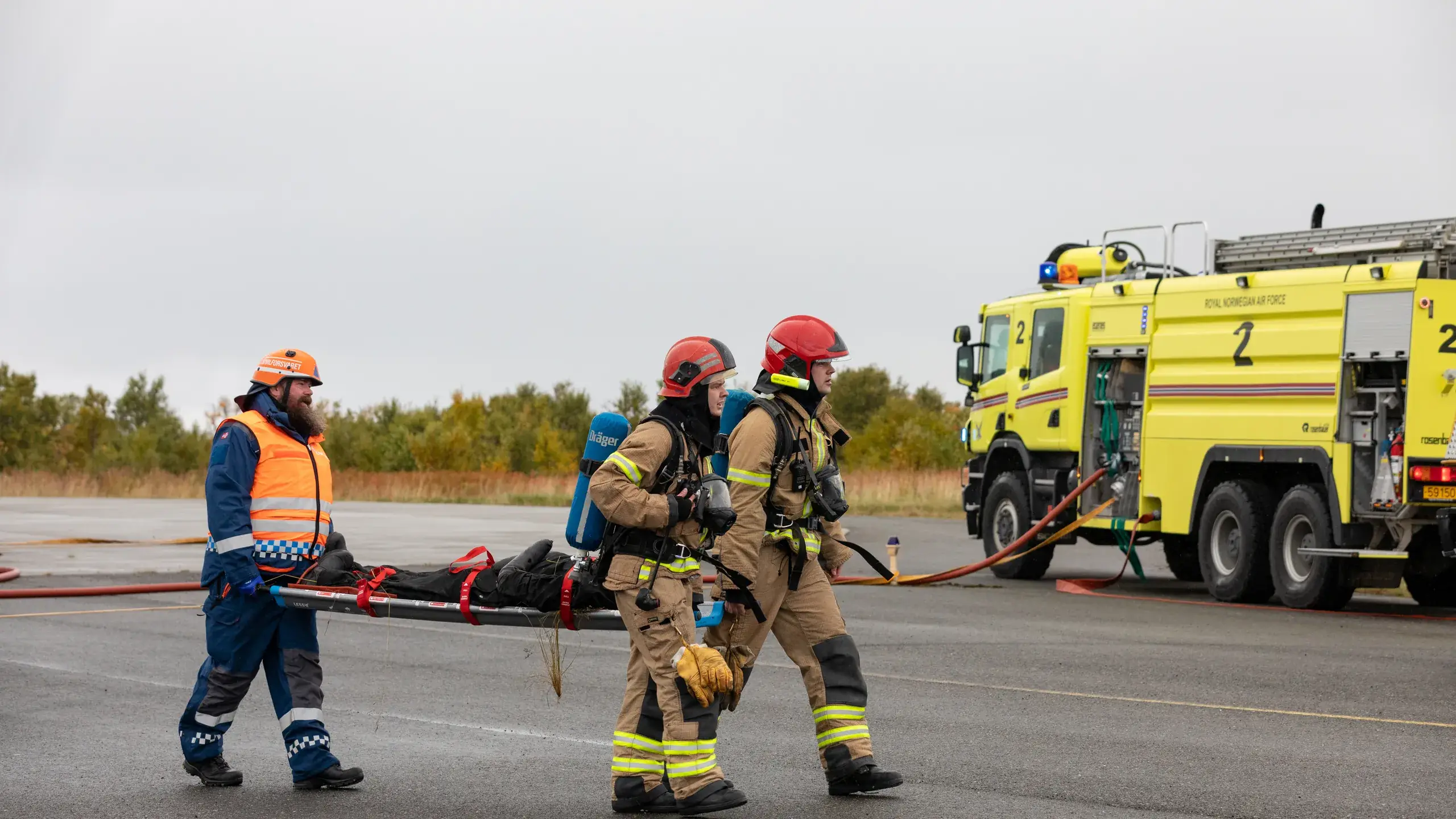 Sivilforsvaret og brannmannskap bærer en øvingspasient på en LESS-båre med blå håndtak.
